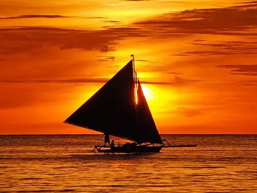 A sailing boat silhouetted against a tropical sunset