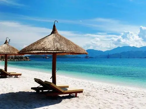 A thatched parasol shading two loungers on white tropical sand