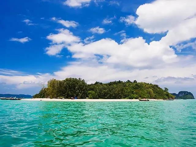 Longtail boats moored off a tree-covered island in the Andaman Sea